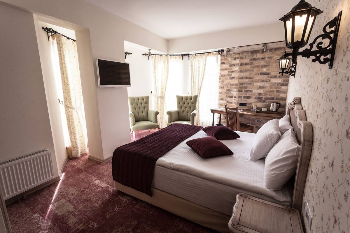 A bedroom with a large bed, a chair, a table, and a TV mounted on the wall.
