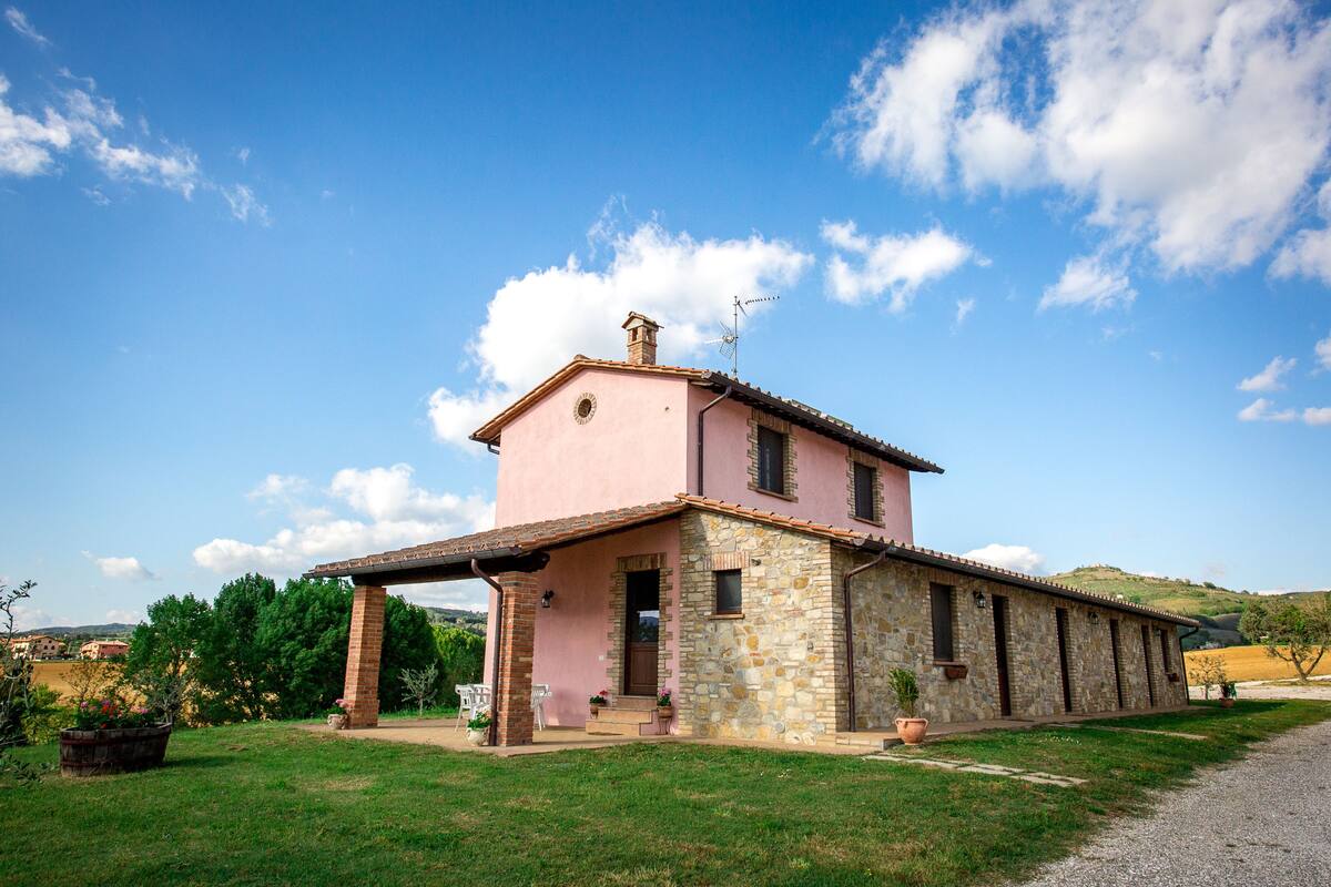 A pink and stone house with a covered porch, a chimney, and a view of the countryside.
