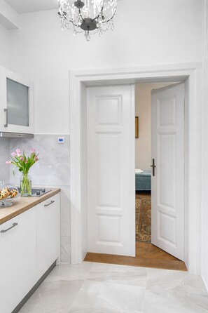 A hallway with white doors, a kitchen area with a microwave, and a chandelier.