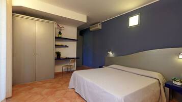 A bedroom with a bed, a desk, a chair, a wardrobe, and a small shelf with plants.