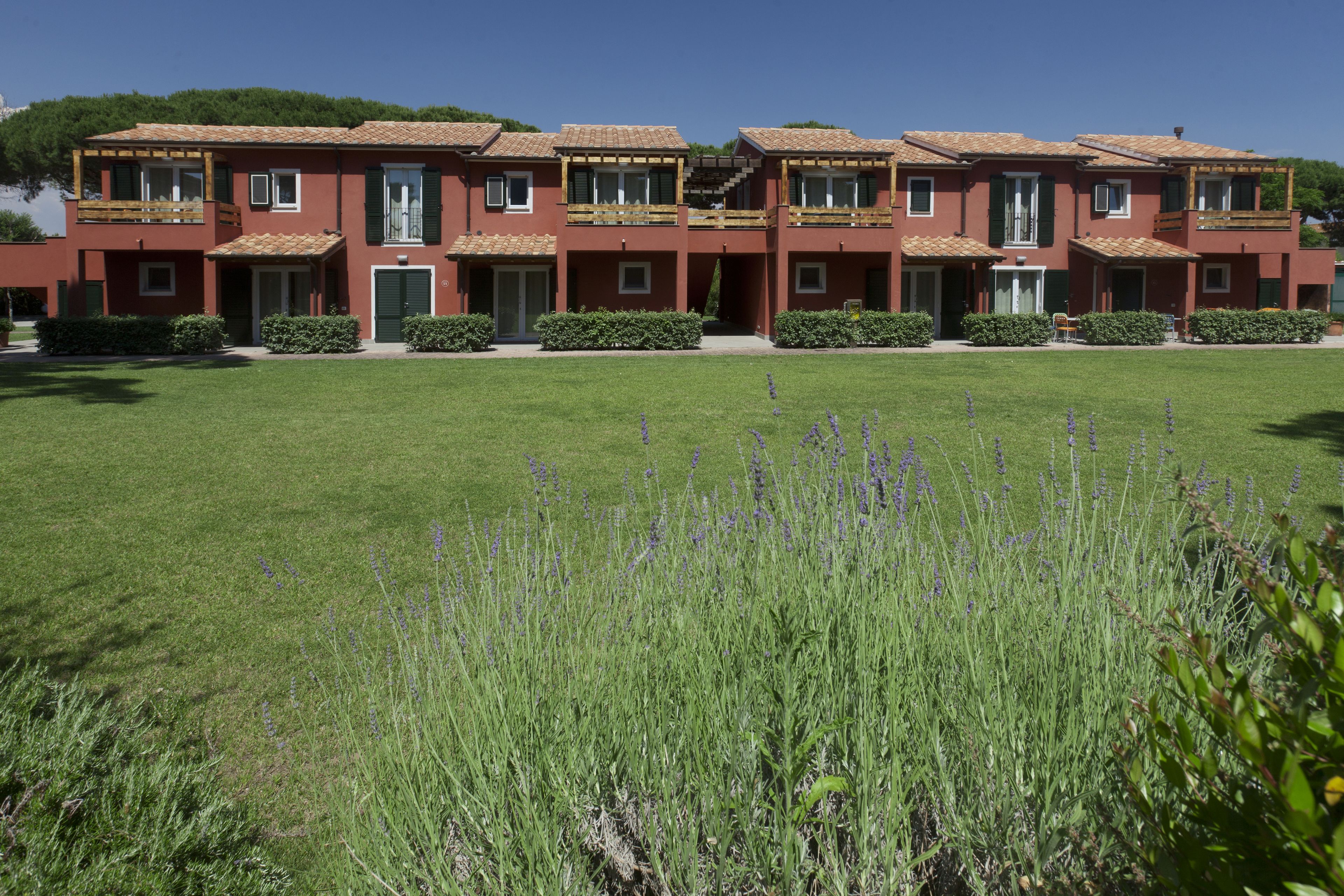 Une rangée de bâtiments rouges aux volets verts, avec une pelouse bien entretenue et des plants de lavande au premier plan.