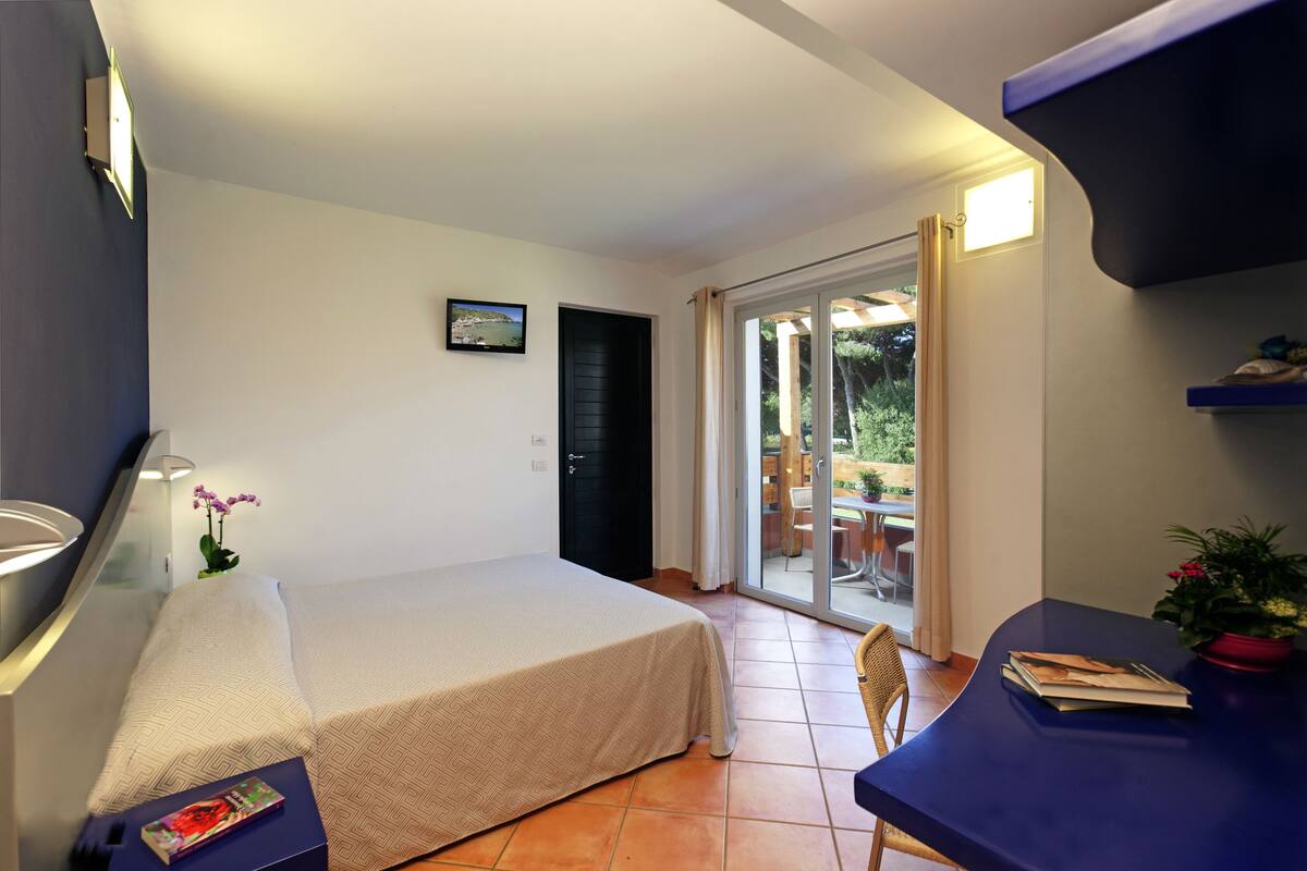 A bedroom with a bed, a desk, a chair, a window, and a door.