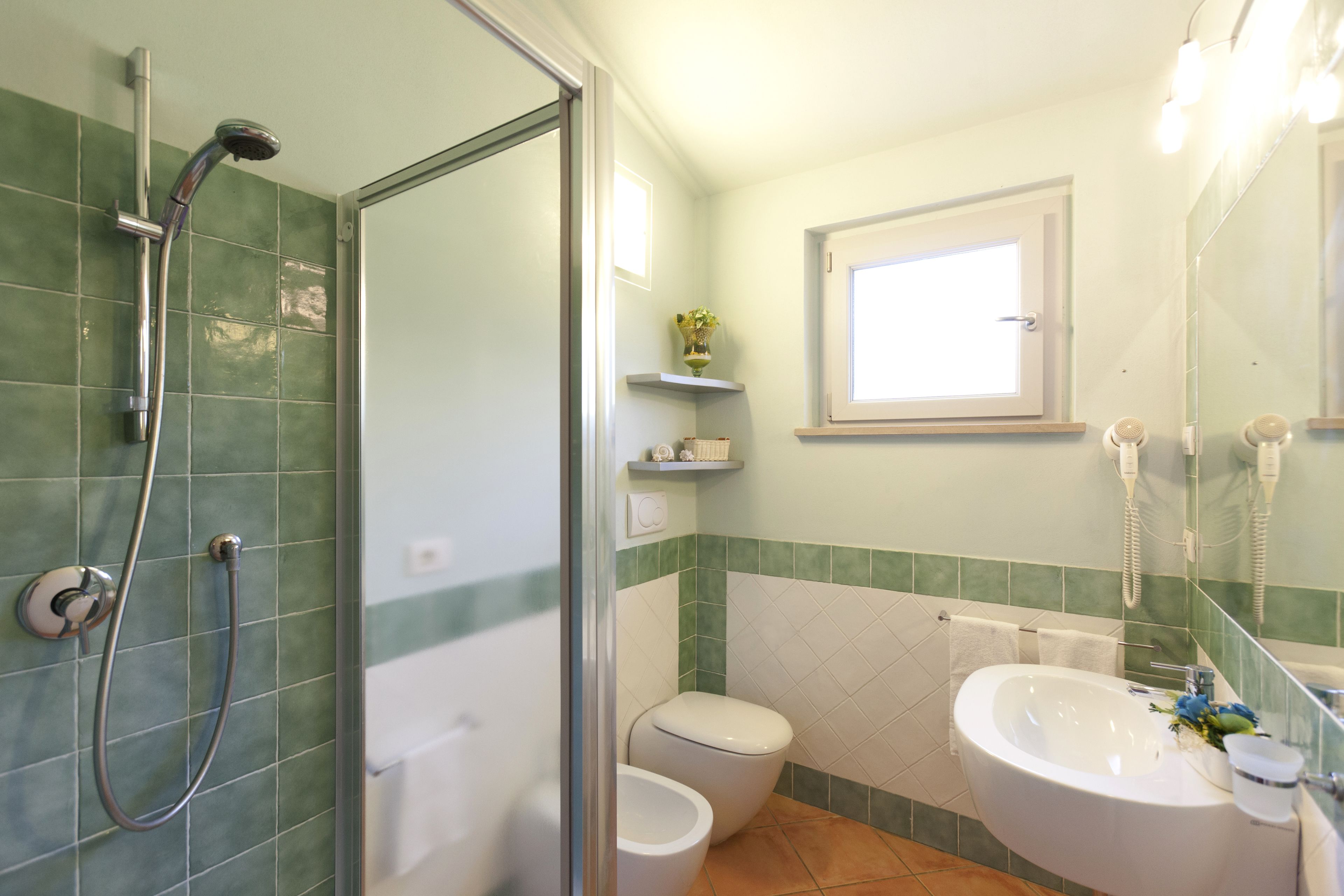 A bathroom with a shower, toilet, sink, and a window.