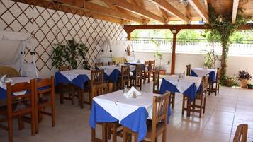 Un espace extérieur aménagé en terrasse, avec des tables et des chaises en bois, surmonté d’une structure de toit en bois.