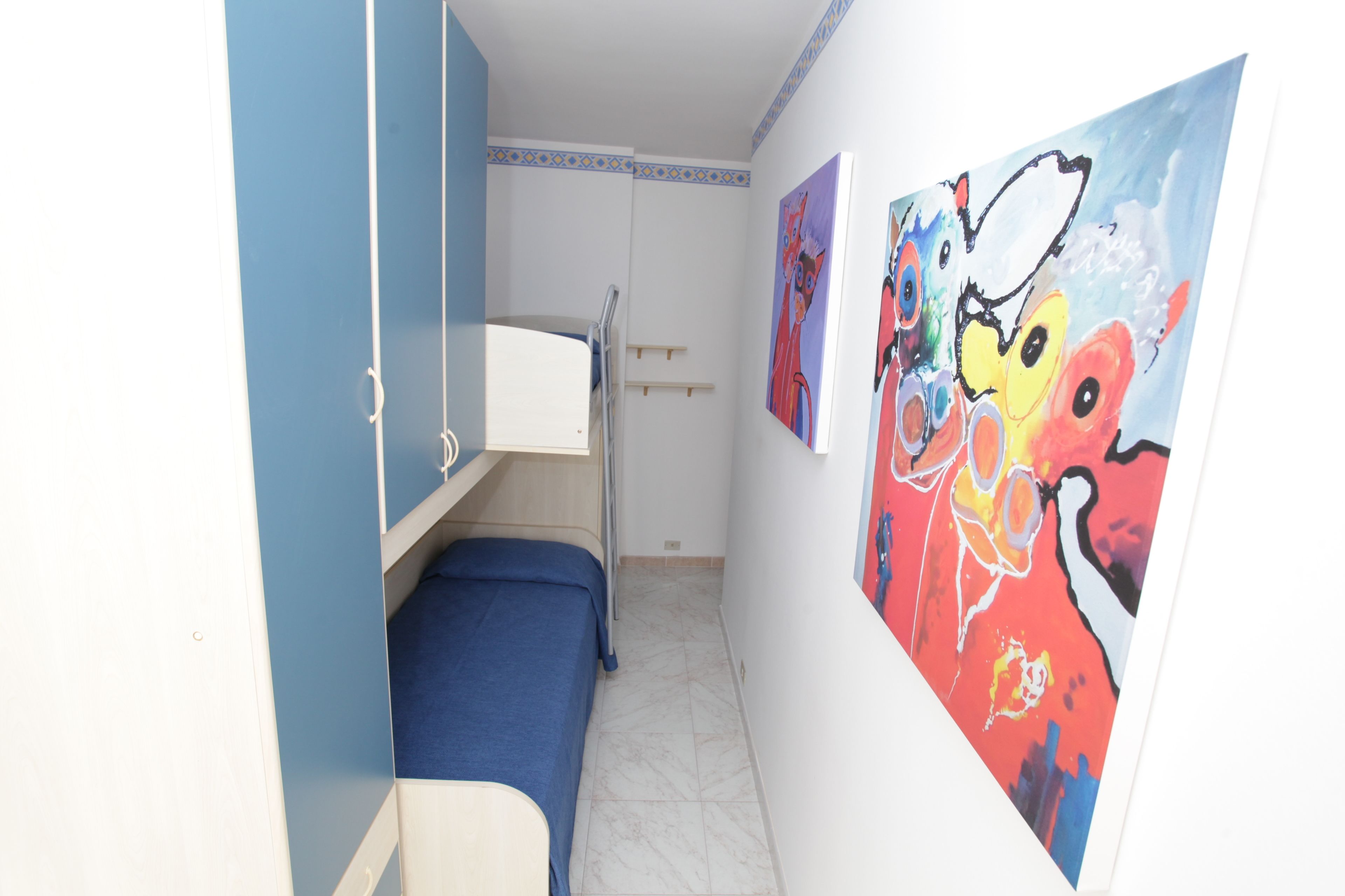 Habitación pequeña con literas, una mesita y una pared decorada con cuadros abstractos coloridos.
