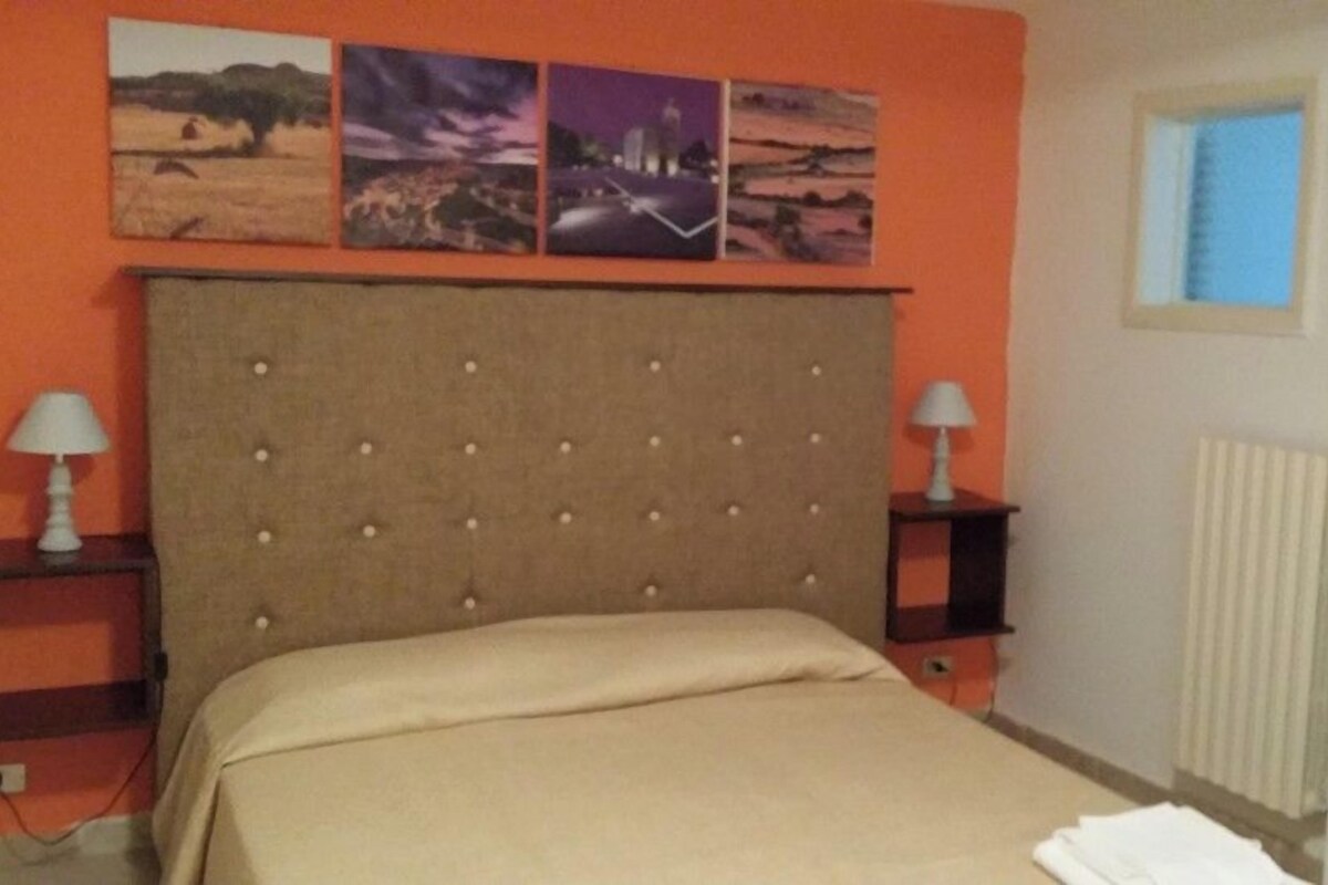 A bedroom with a large bed, two bedside tables, a radiator, and three wall-mounted pictures.