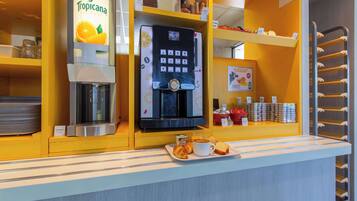 A coffee station with a Tropicana juice dispenser, a coffee machine, and a selection of pastries and bread.