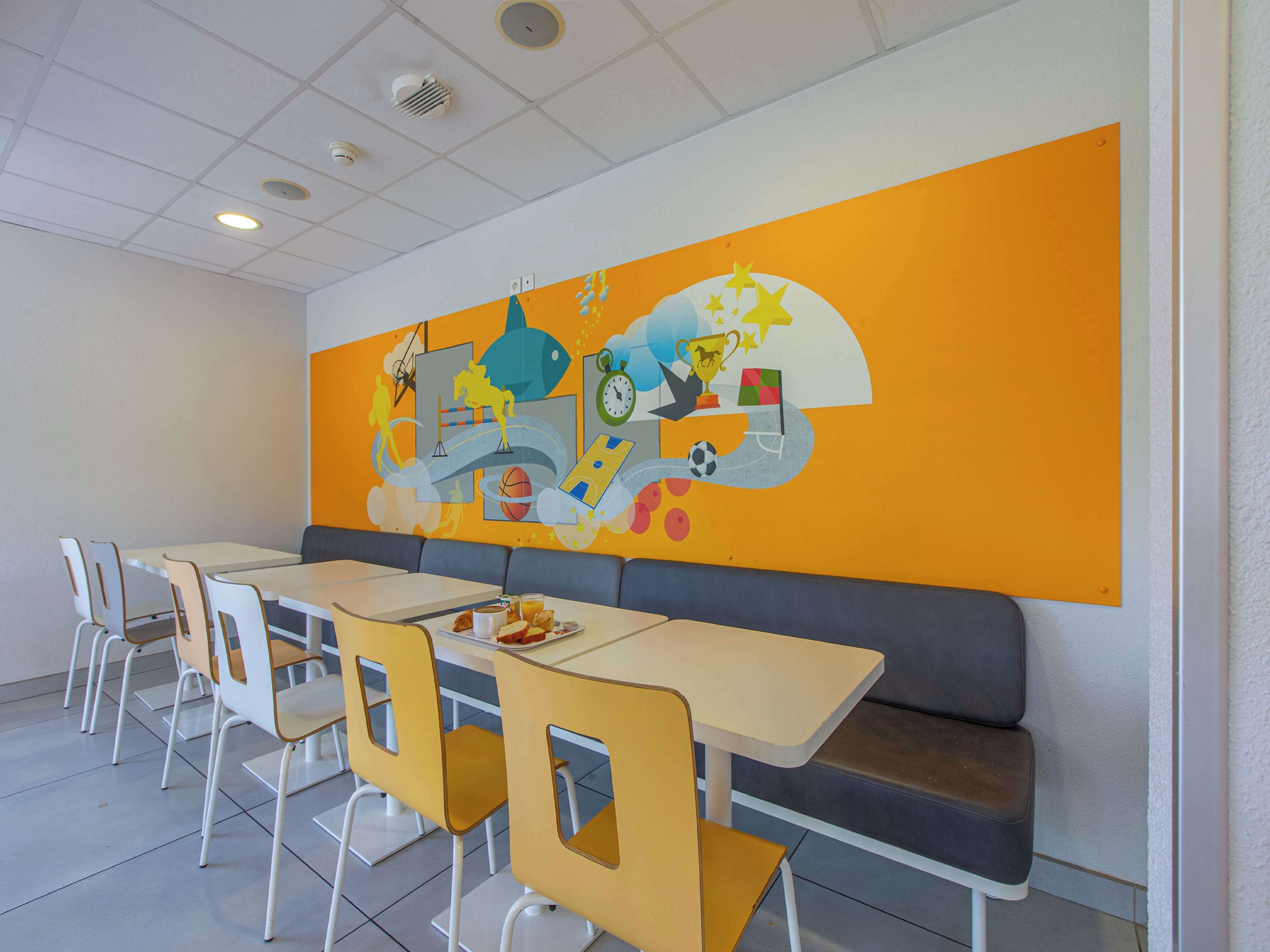 Un espace repas agrémenté d’une fresque murale, de tables et de chaises.