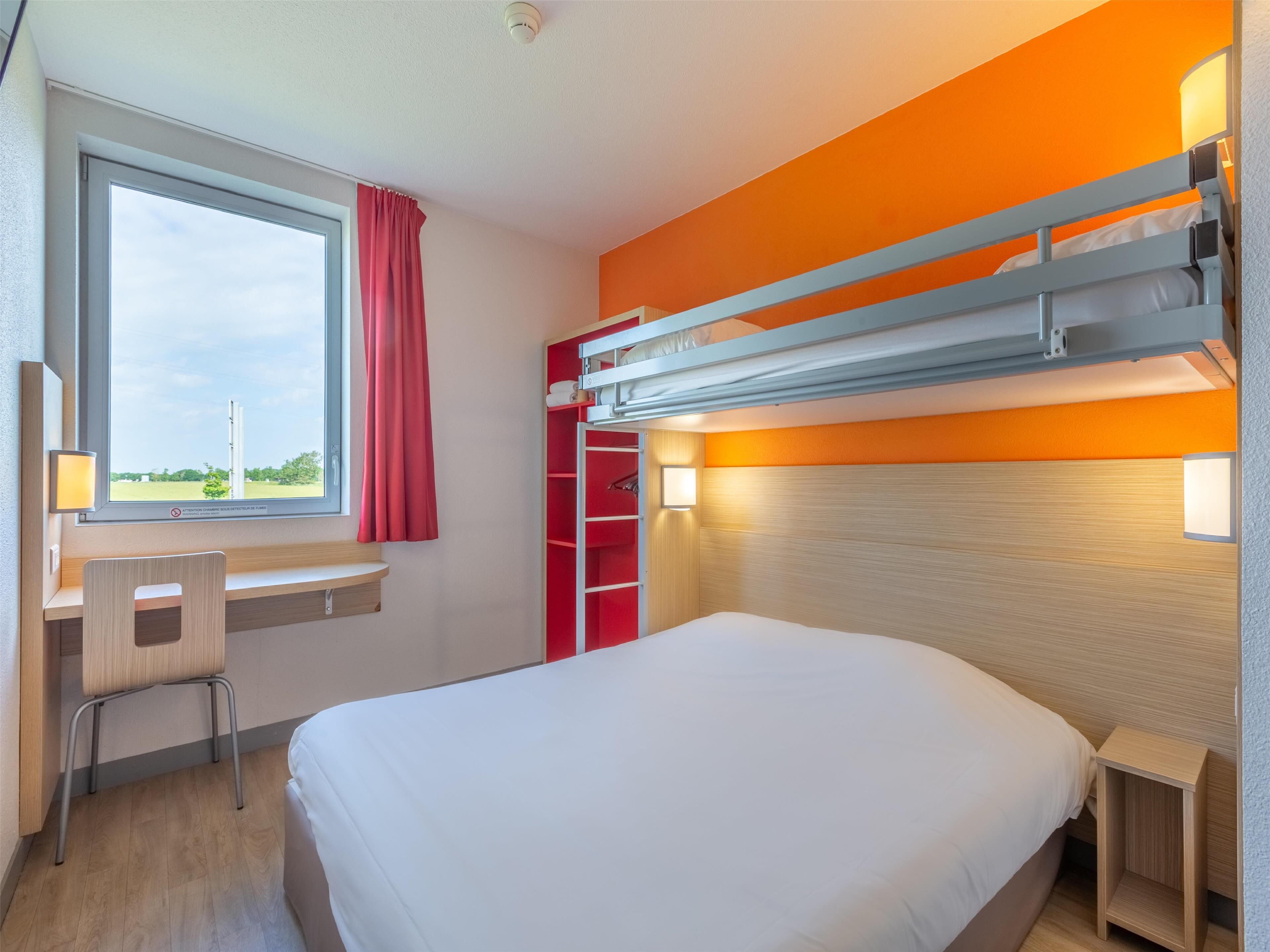 Une chambre d’hôtel avec un lit superposé, un bureau avec une chaise, une fenêtre avec un rideau et une vue sur l’extérieur.