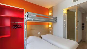 Habitación de hotel con dos camas, un mueble rojo con ropa y una cama litera.