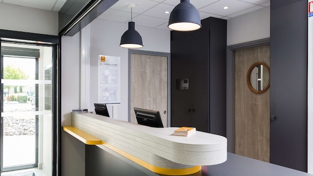 Een receptiebalie met een gebogen ontwerp, twee hanglampen, een houten deur en een prikbord met mededelingen.