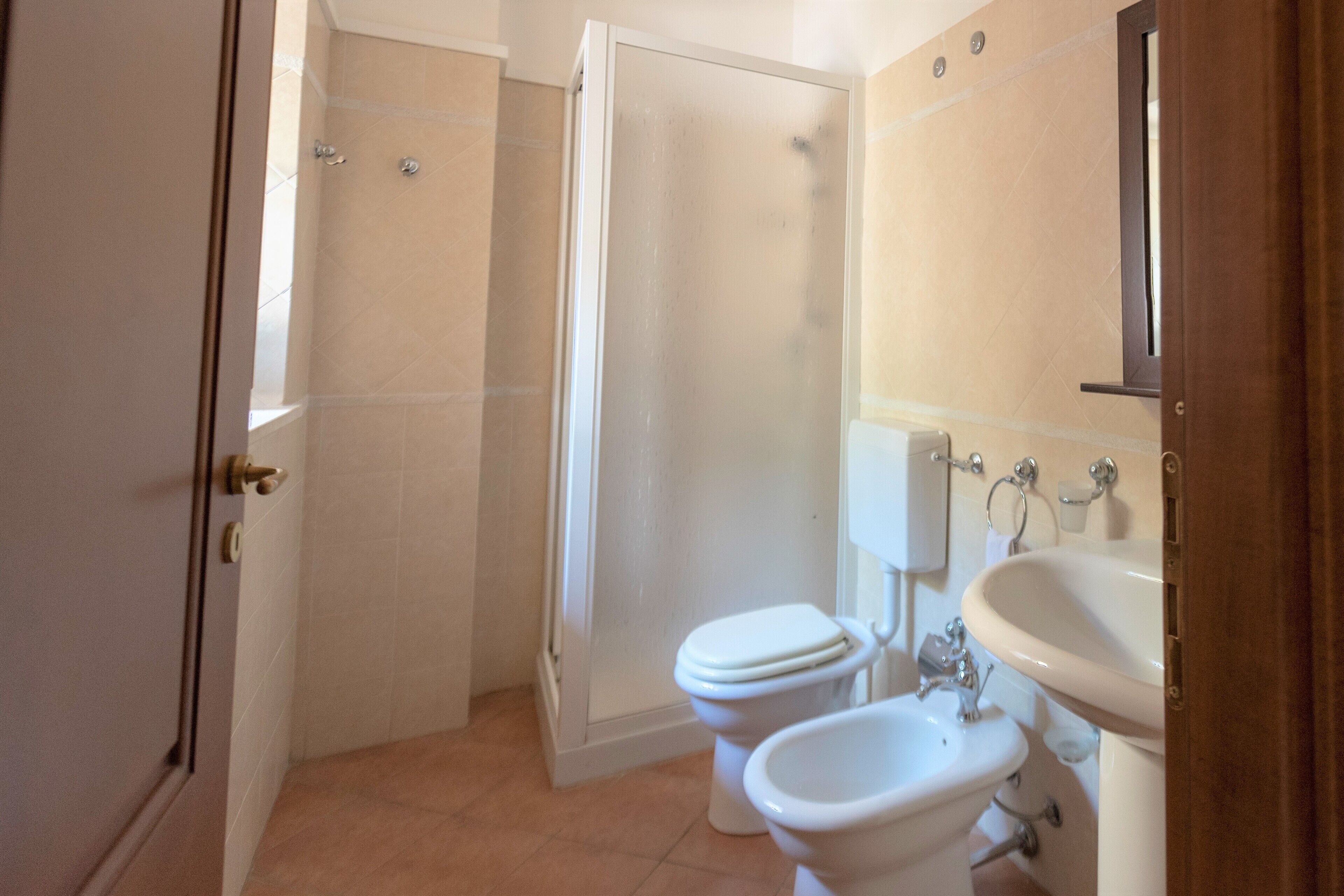 A bathroom with a shower, toilet, bidet, and sink.