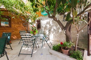 Un patio con una mesa y sillas, rodeado de plantas en macetas y un árbol.