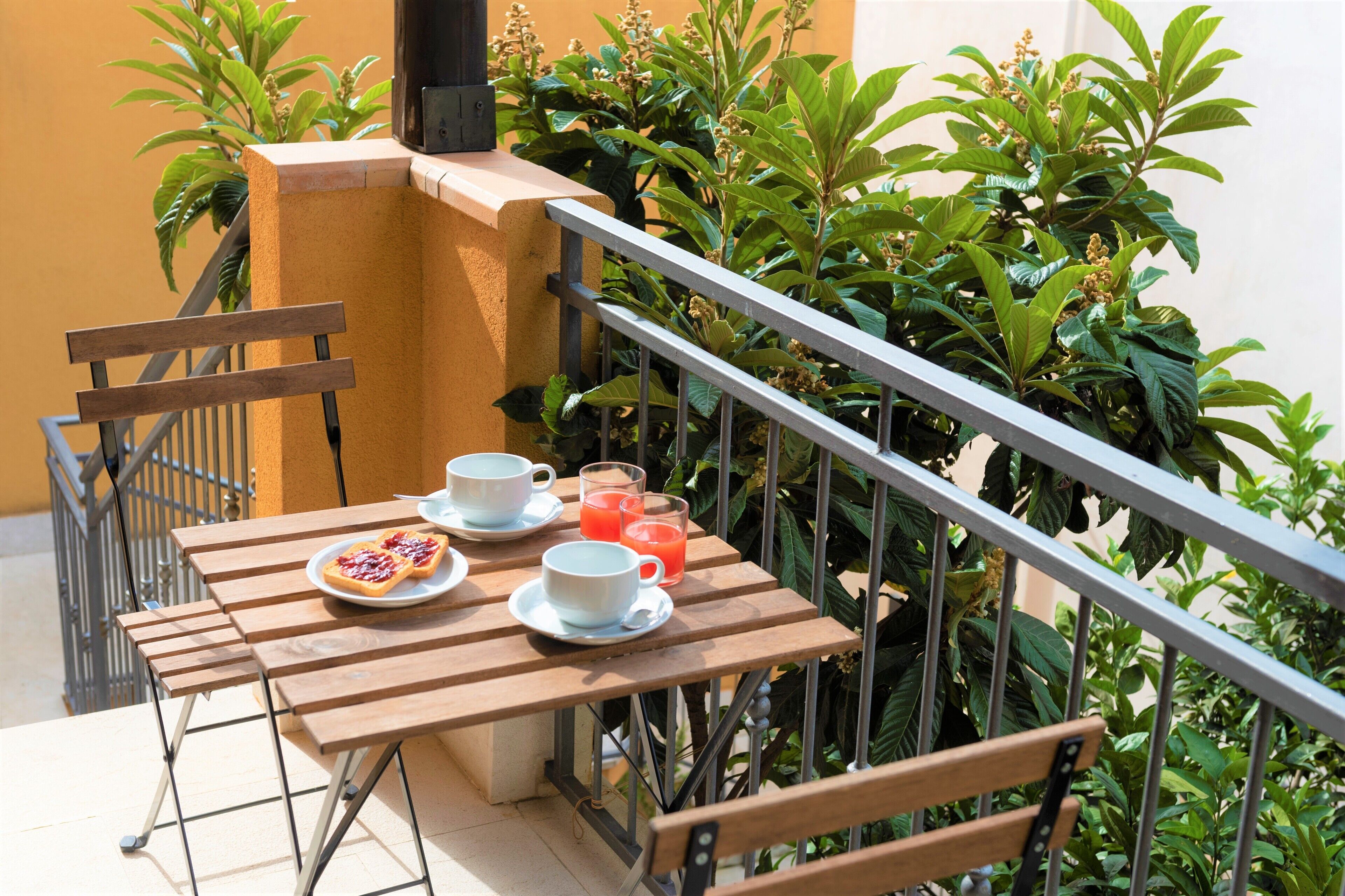 Una mesa de madera con un plato de comida y dos tazas, frente a una pared amarilla con plantas verdes al fondo.