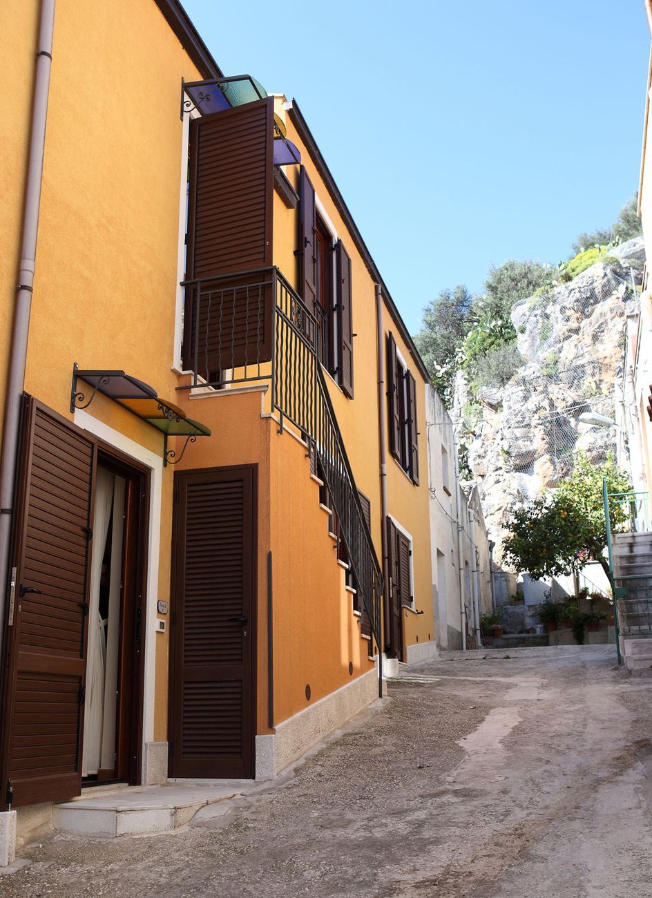 A narrow street with buildings on either side, a clear sky, and a rocky hill in the background.