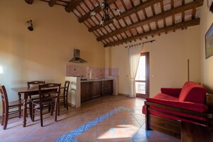 Amplia sala de estar con mesa de comedor de madera, sillas, sofá rojo y cocina con salpicadero de azulejos.