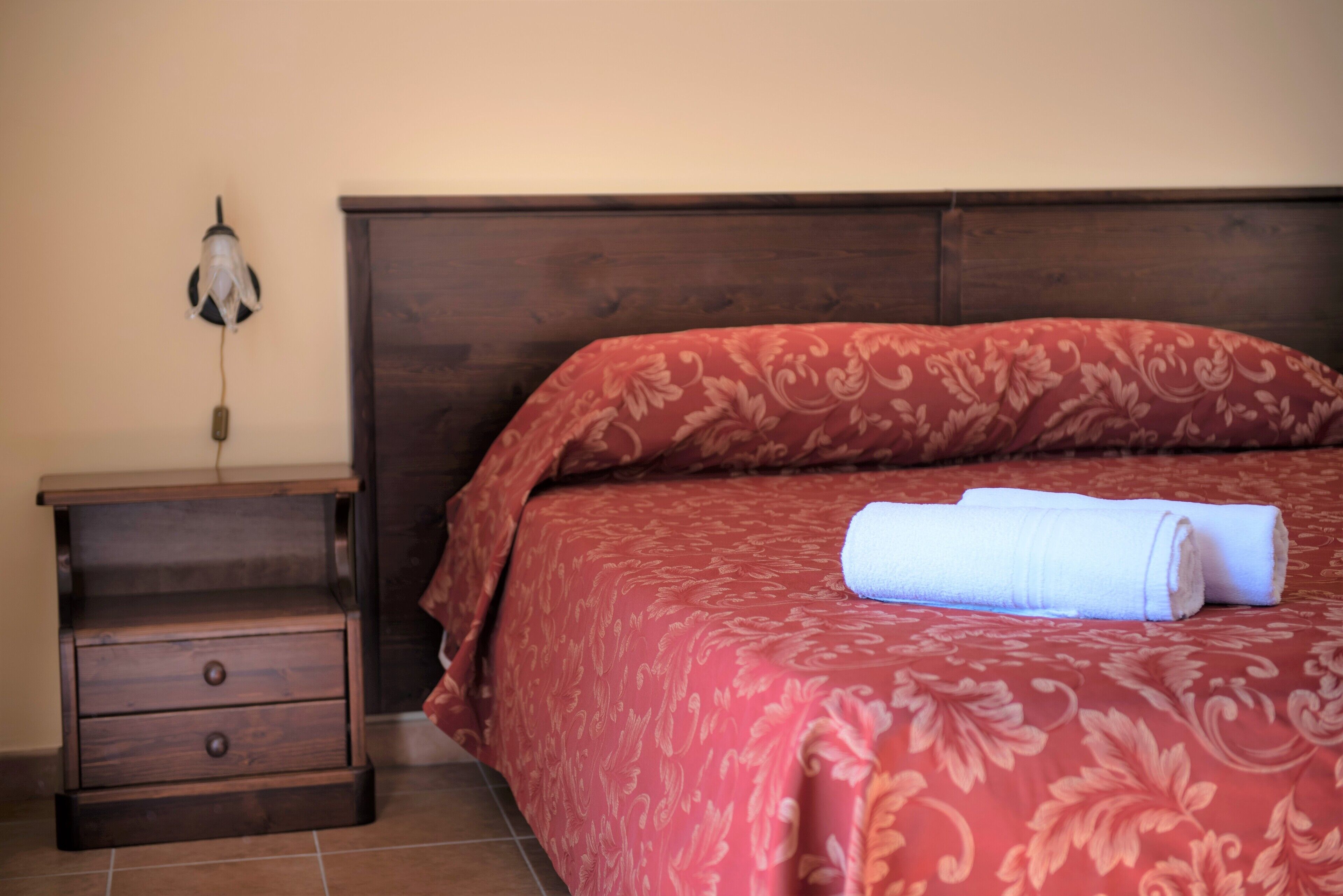 Una cama bien hecha con una colcha floral roja y una toalla blanca doblada.