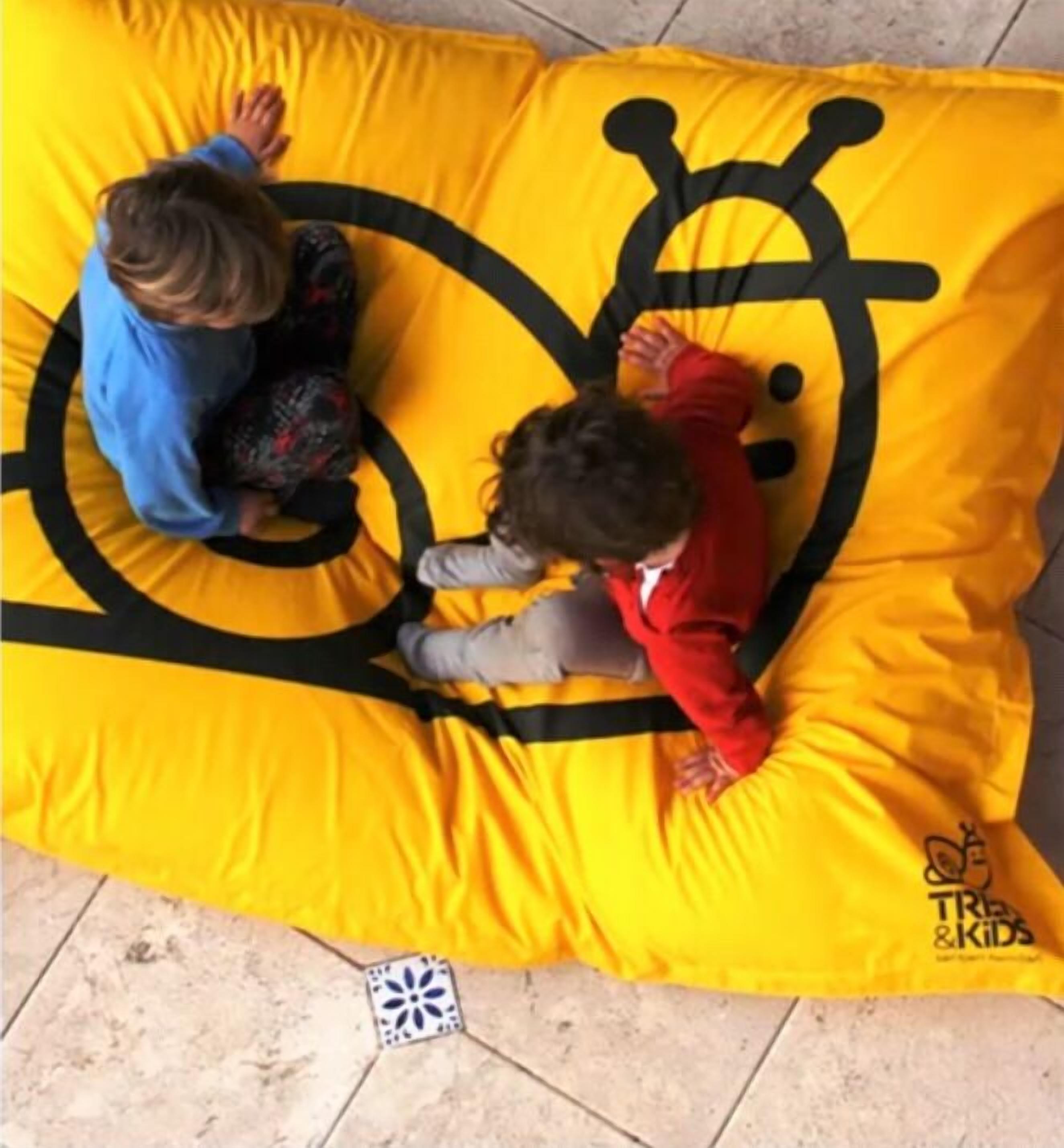 Dos niños jugando en un sillón de mezcla de colores amarillos con un diseño de carita sonriente negra.