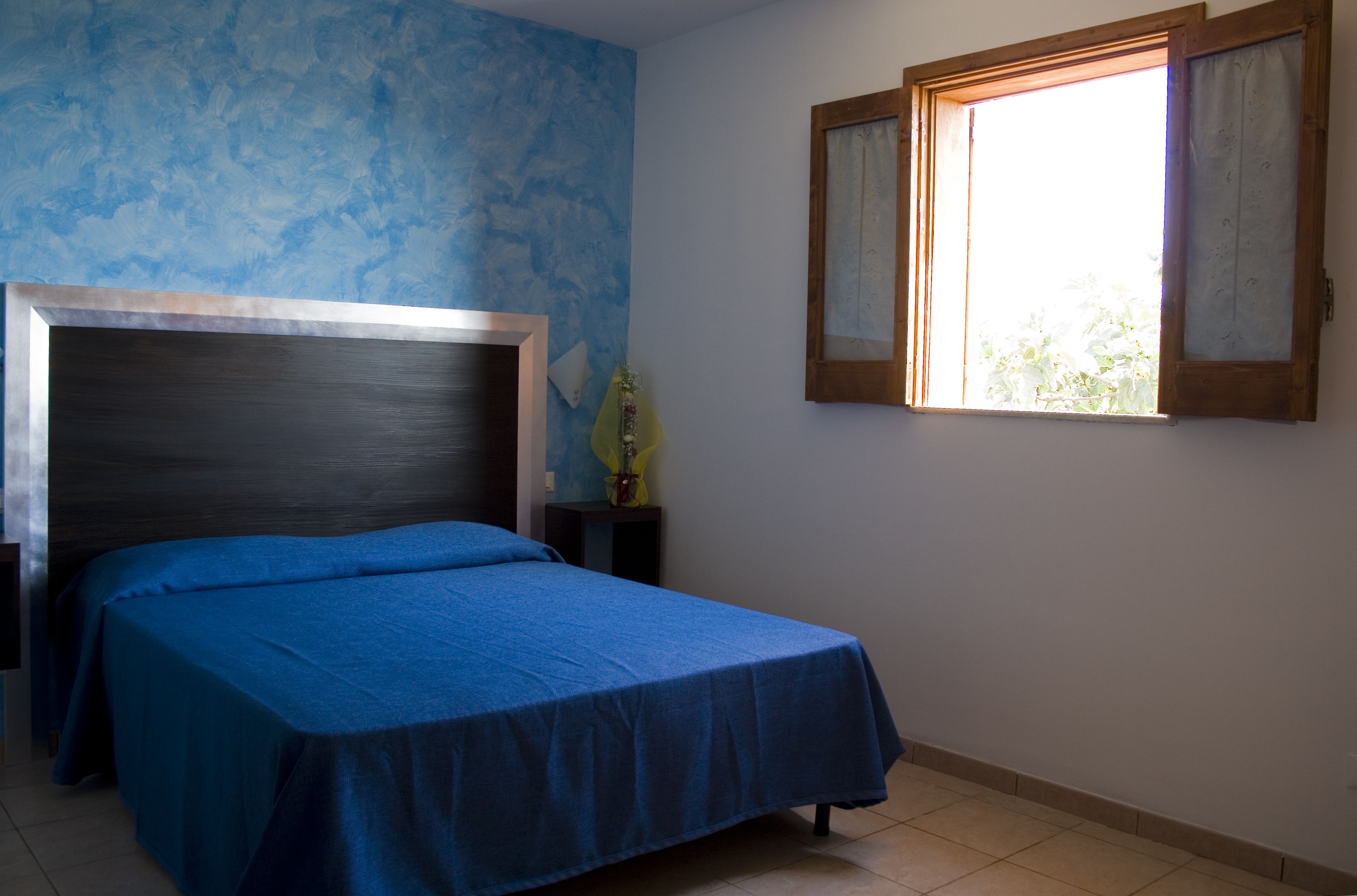 A bedroom with a bed, a nightstand, a window, and a wall with a blue pattern.