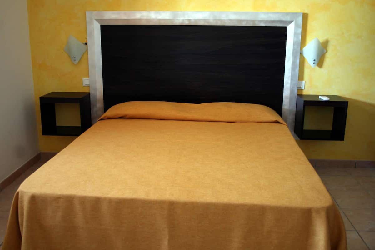 A bed with a headboard, two bedside tables, and a wall-mounted light fixture.