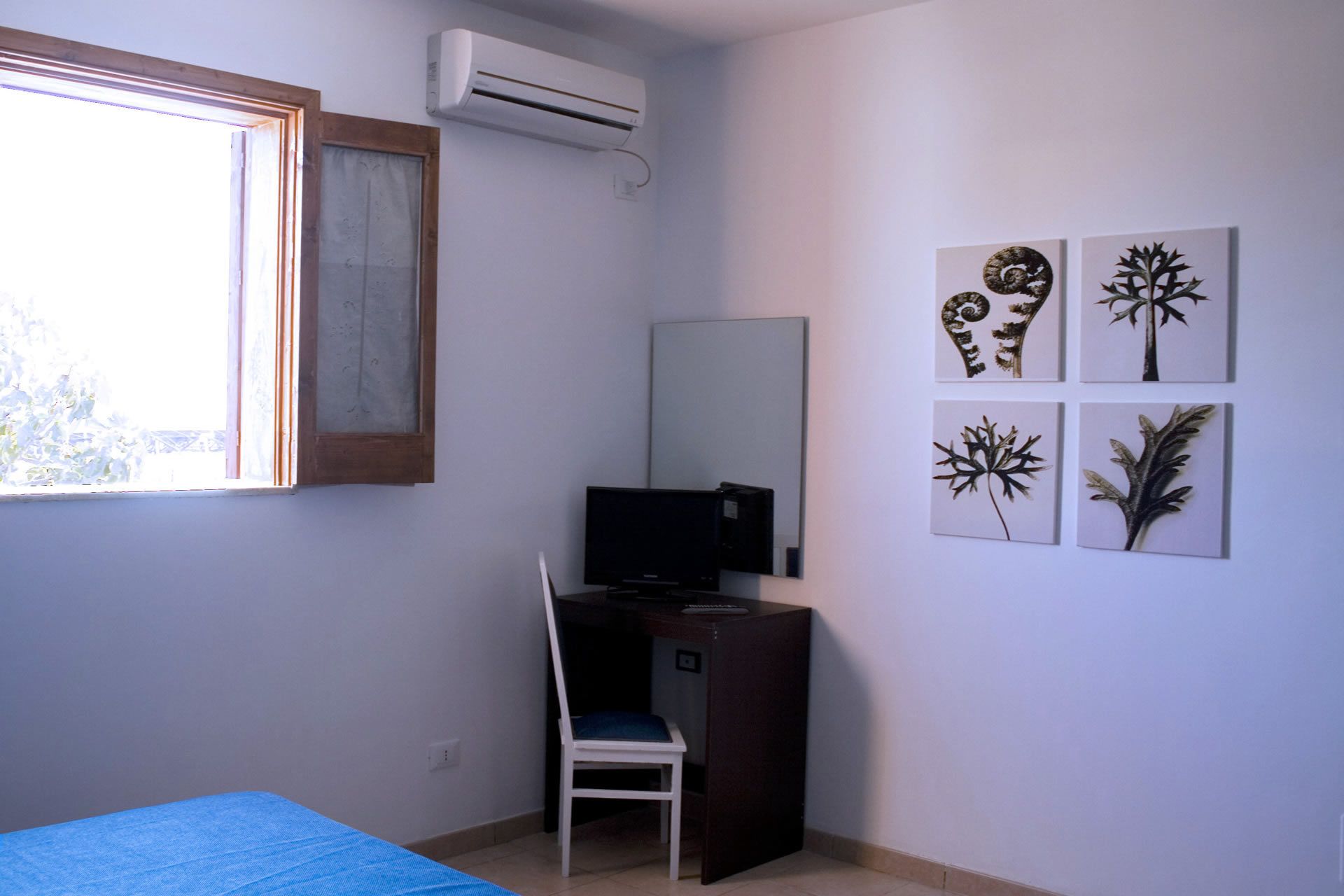 Ein Zimmer mit einem Bett, einem Schreibtisch mit Stuhl, einer Klimaanlage und Wandbildern.
