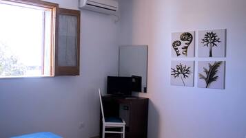 Ein Zimmer mit einem Bett, einem Schreibtisch mit Stuhl, einer Klimaanlage und Wandbildern.