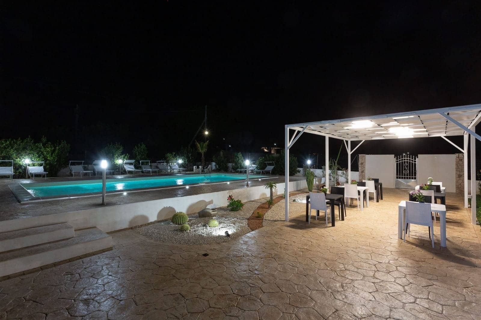 A nighttime outdoor pool area with a covered seating area and lounge chairs.
