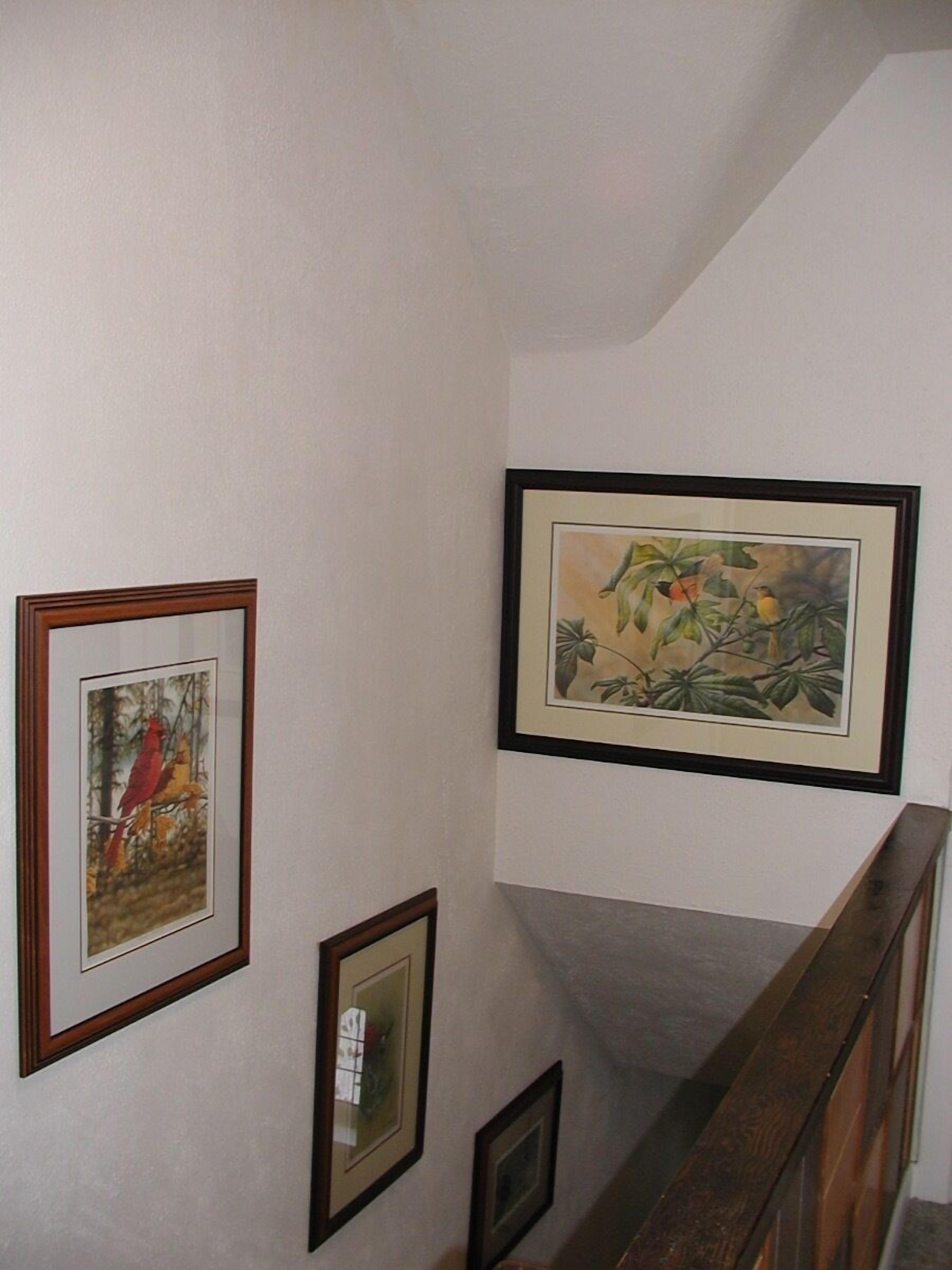 Una escalera con barandilla de madera y una pared decorada con cuadros.