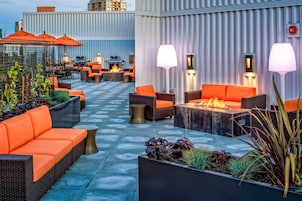 Un espace extérieur aménagé avec des canapés et des tables orange, un foyer et un éclairage d’ambiance.