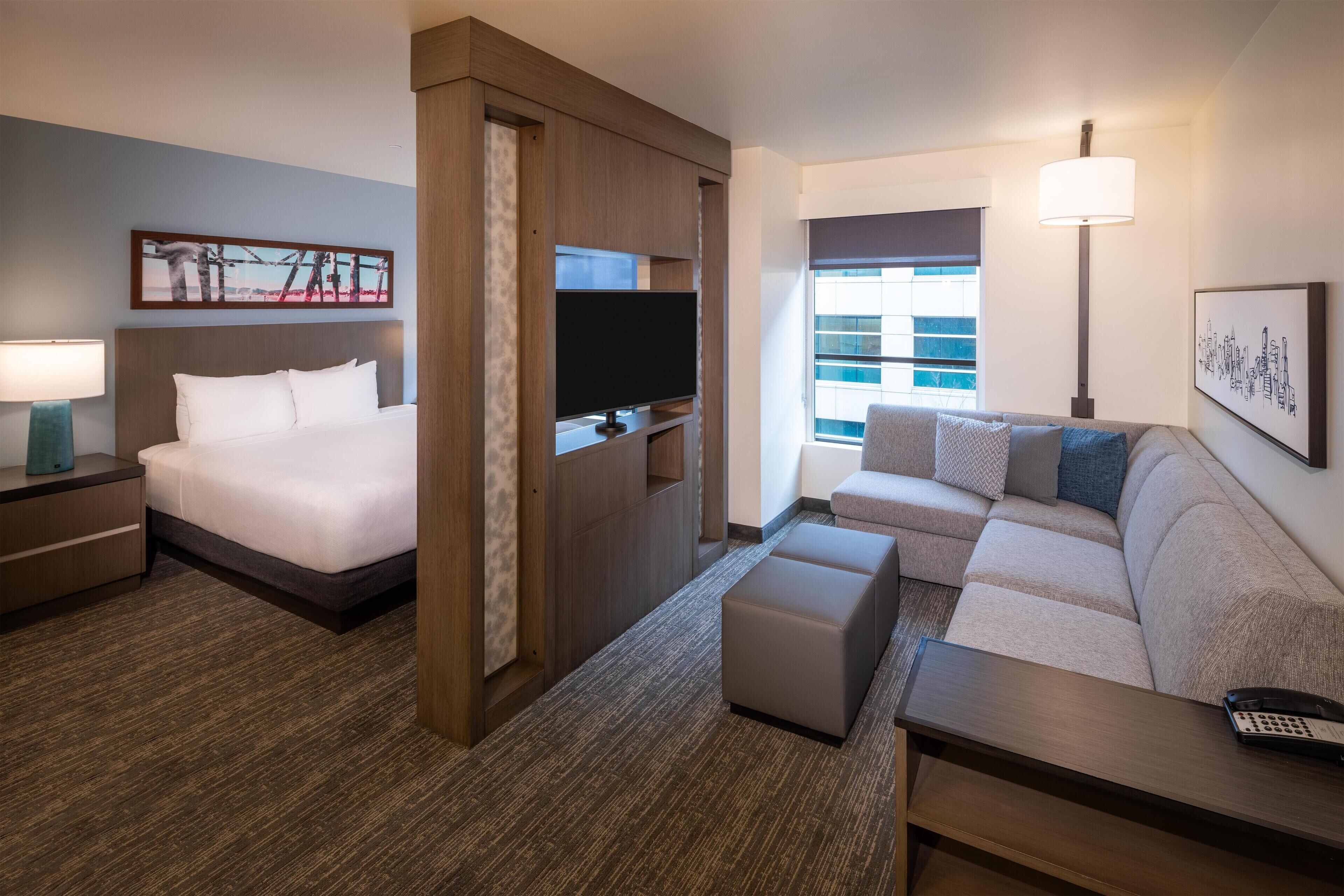 Una habitación de hotel con cama, televisor, sofá, mesa de centro y lámpara.