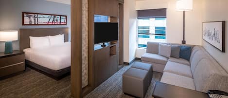 Una habitación de hotel con cama, televisor, sofá, mesa de centro y lámpara.