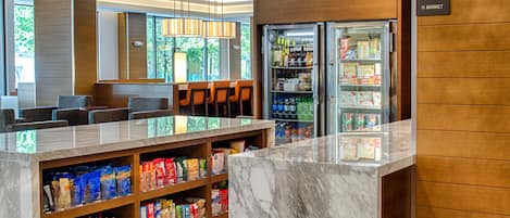 Un hall de hotel con mostrador de recepción de mármol, zona de estar y vitrina refrigerada.