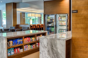 Un hall de hotel con mostrador de recepción de mármol, zona de estar y vitrina refrigerada.