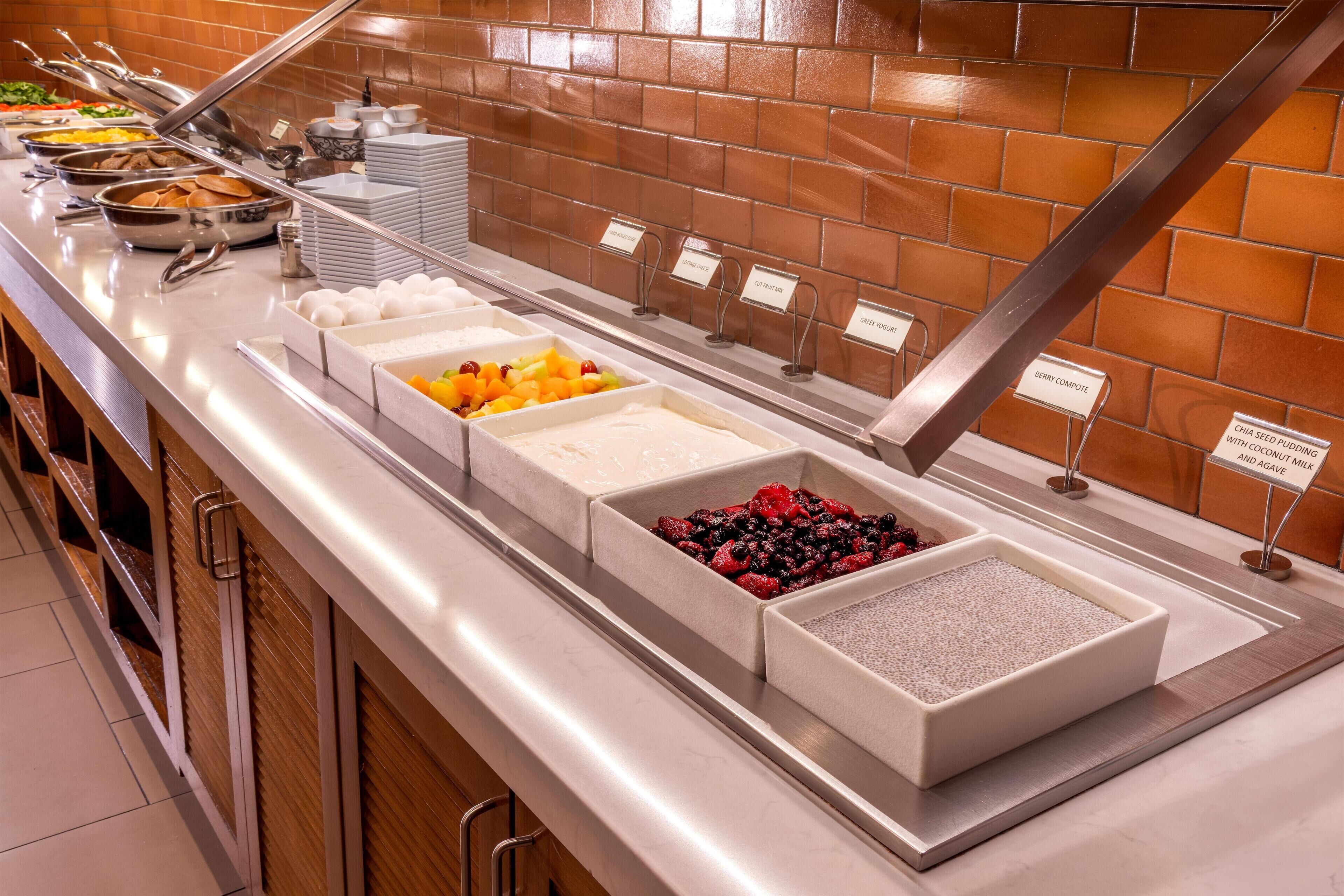 A buffet with labeled food stations including fruits, yogurt, and cereal.