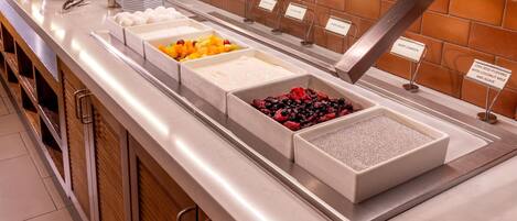 A buffet with labeled food stations including fruits, yogurt, and cereal.
