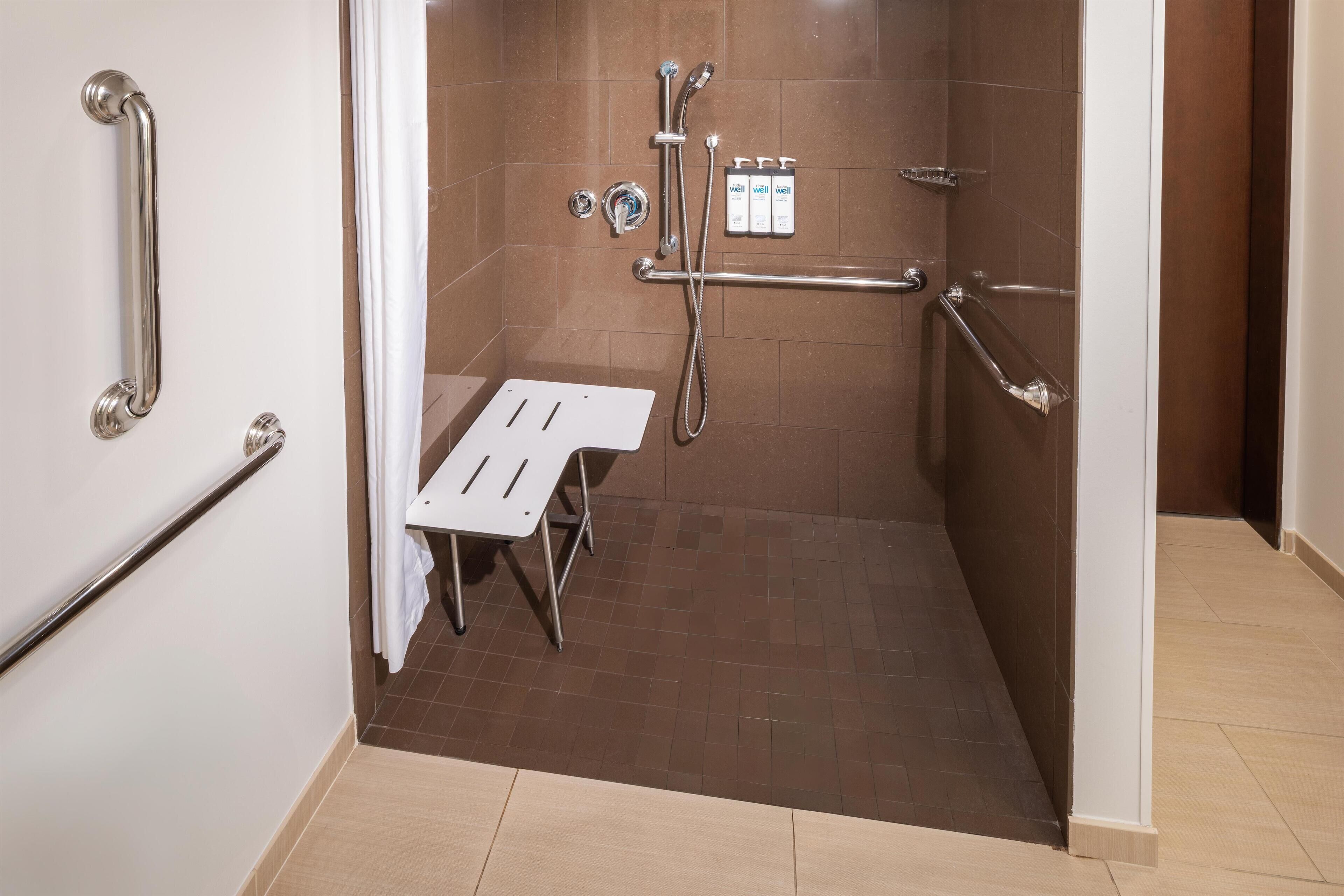 A bathroom with a shower, grab bars, and a white sink.