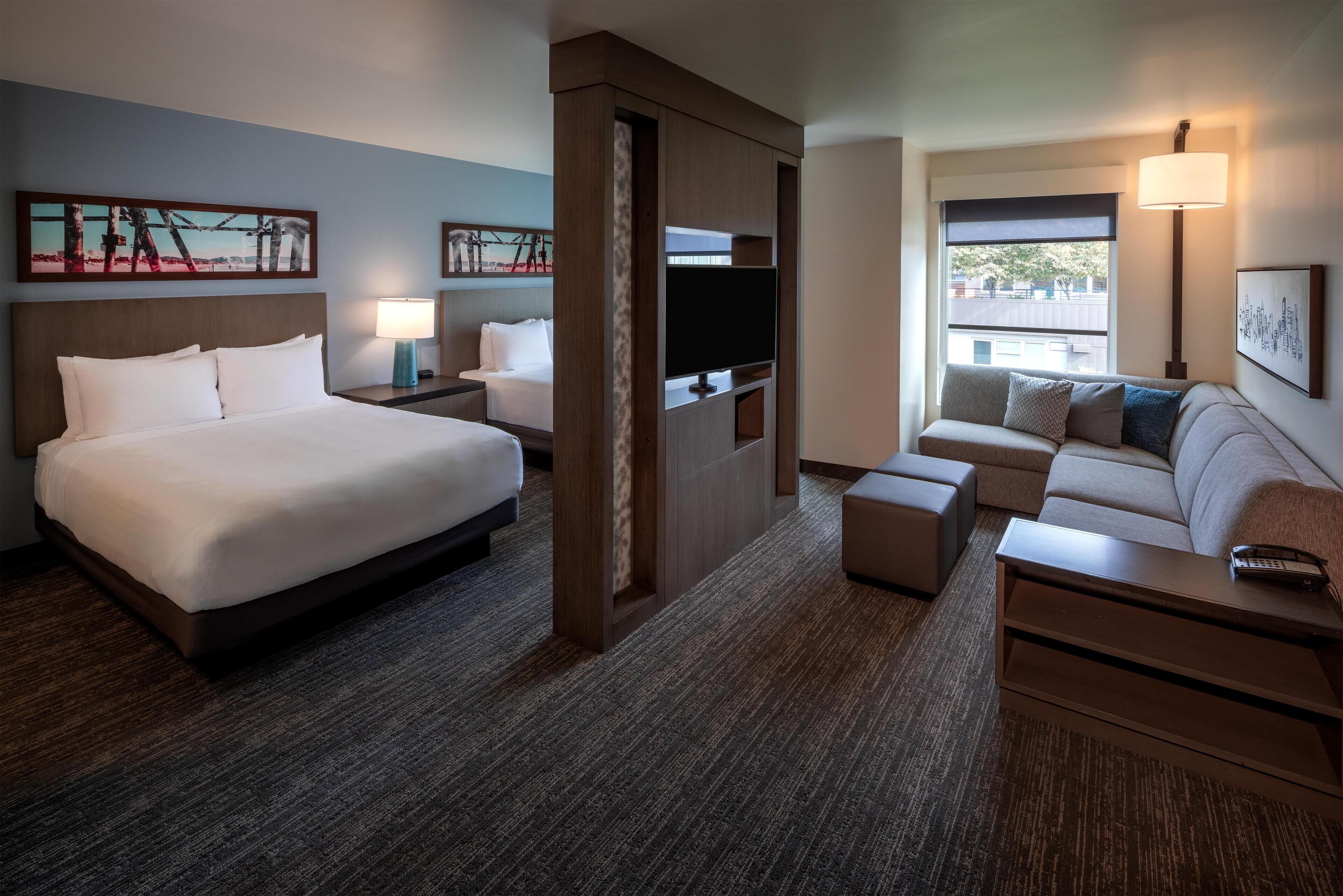 A hotel room with a large bed, a sofa, a TV, and artwork on the walls.