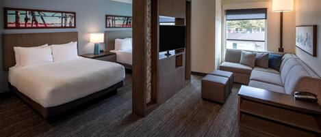 A hotel room with a large bed, a sofa, a TV, and artwork on the walls.