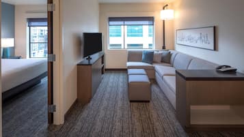 A hotel room with a bed, a sofa, a TV, a desk, and a window with a city view.