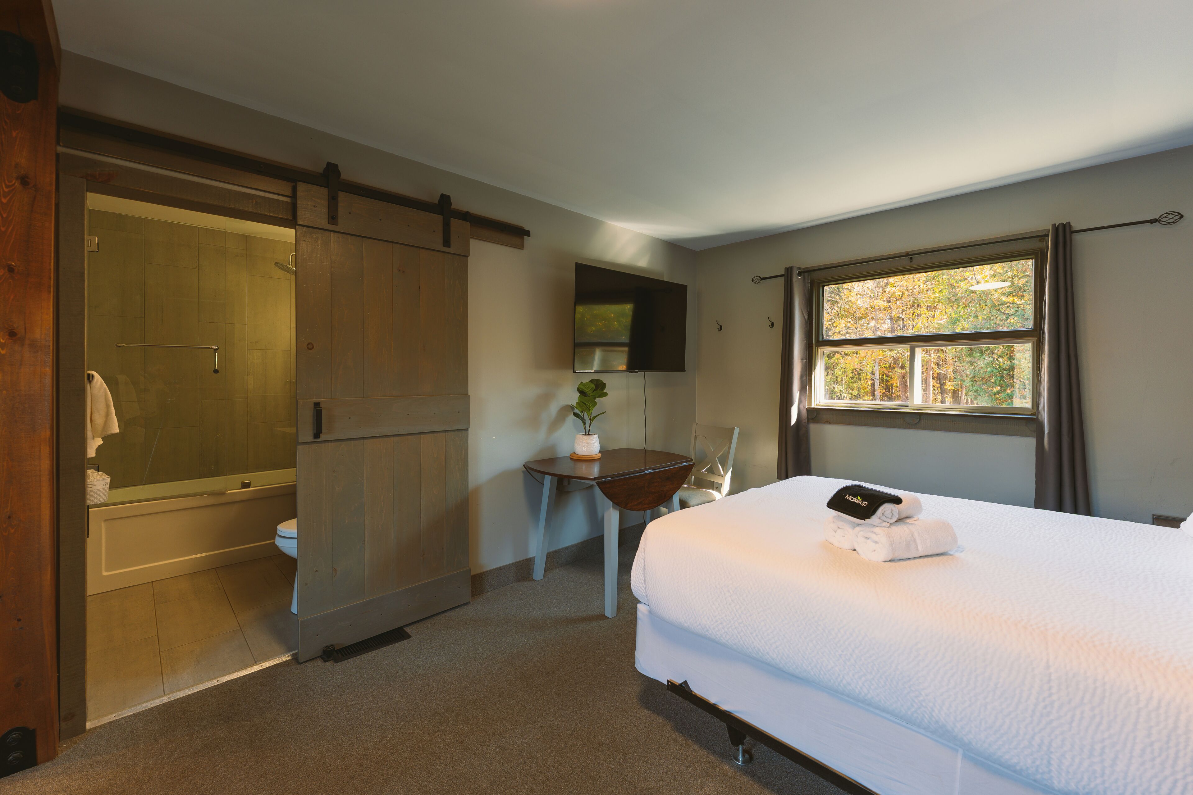 Un dormitorio con cama, escritorio, silla, ventana y puerta corredera.