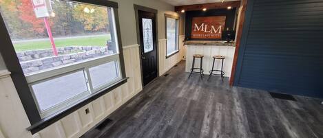 A hotel lobby with a wooden floor, a reception desk, and two bar stools.