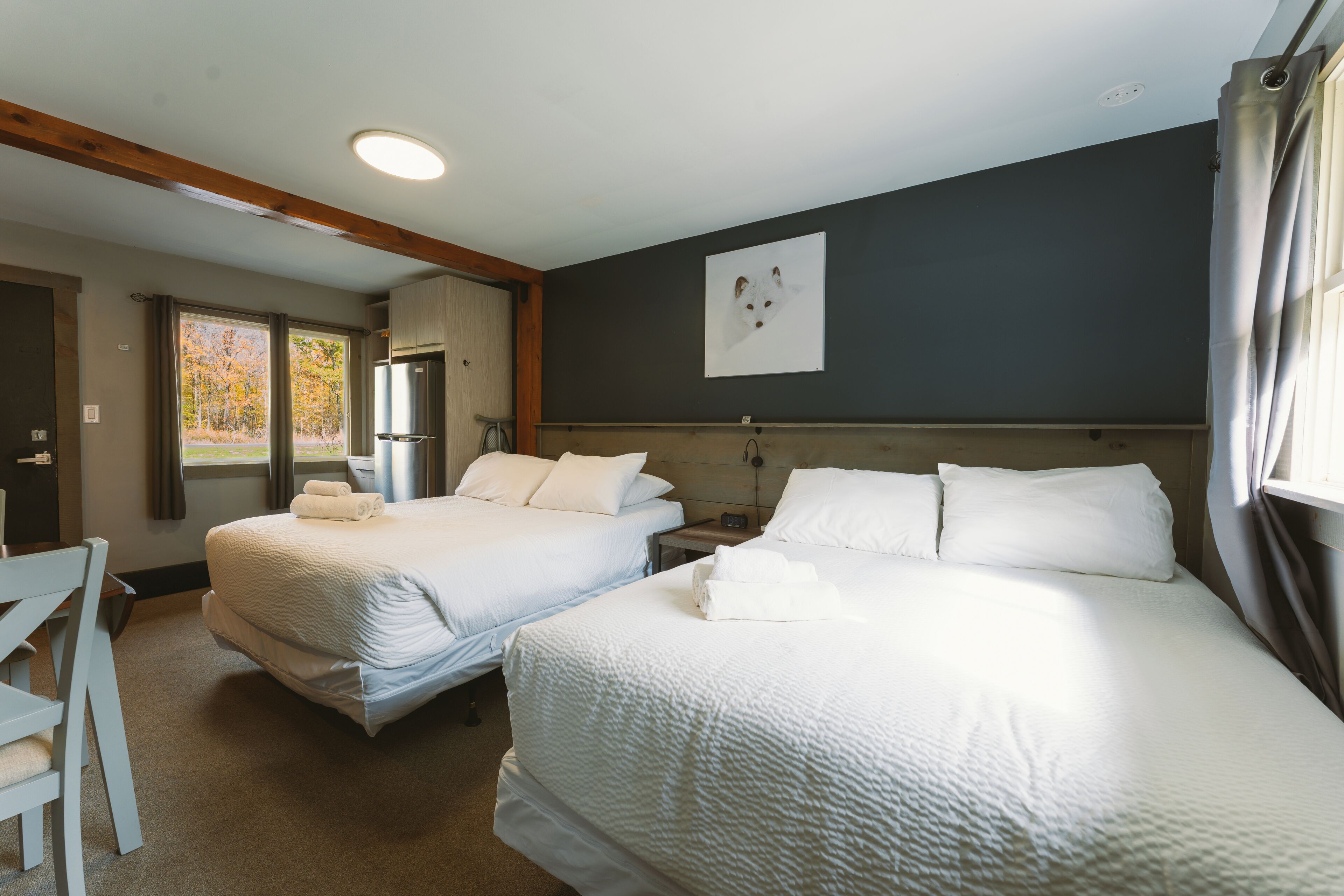 Habitación de hotel con dos camas, un escritorio, un refrigerador y una ventana con cortinas.