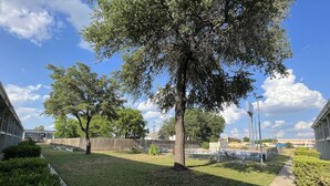 A well-maintained outdoor area with a grassy lawn, a wooden fence, and a large tree providing shade. - Economy Hotel San Antonio  (San Antonio)