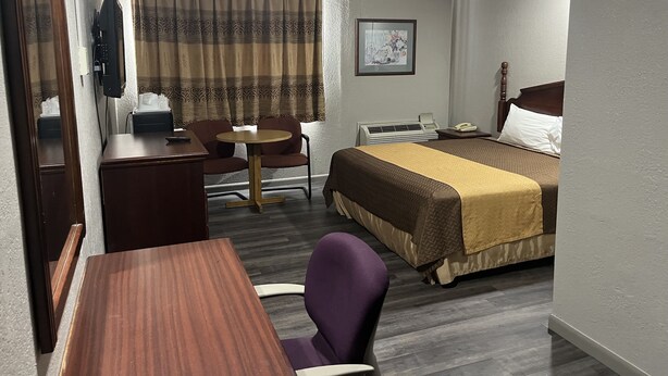 A hotel room with a bed, a desk, a chair, a small table, a telephone, and a window with curtains. - Economy Hotel San Antonio  (San Antonio)