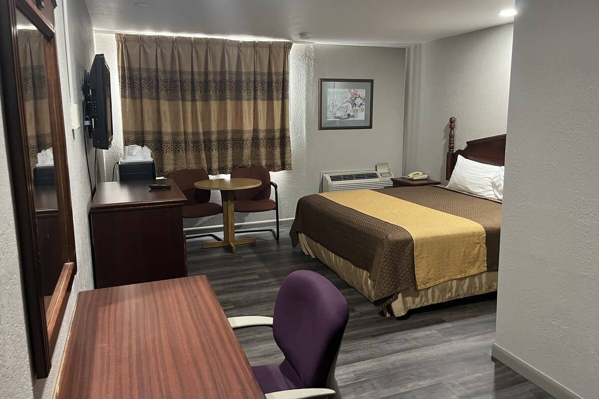 Una habitación de hotel con cama, escritorio, silla, mesita, teléfono y ventana con cortinas.