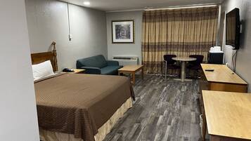 Habitación de hotel con cama, escritorio, silla, mesa, televisor y ventana con cortinas.