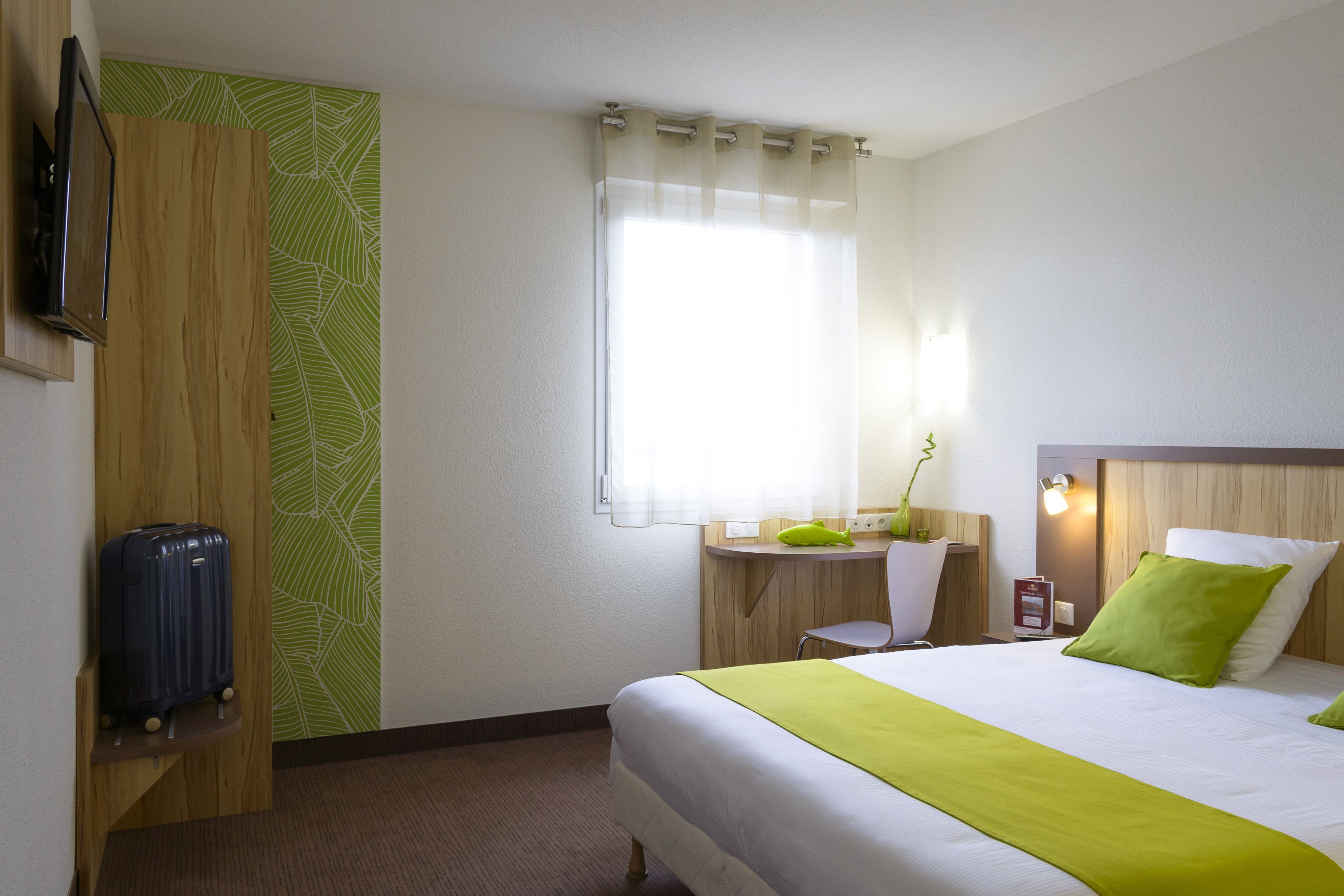 A hotel room with a bed, a desk, a chair, a TV, and a suitcase.