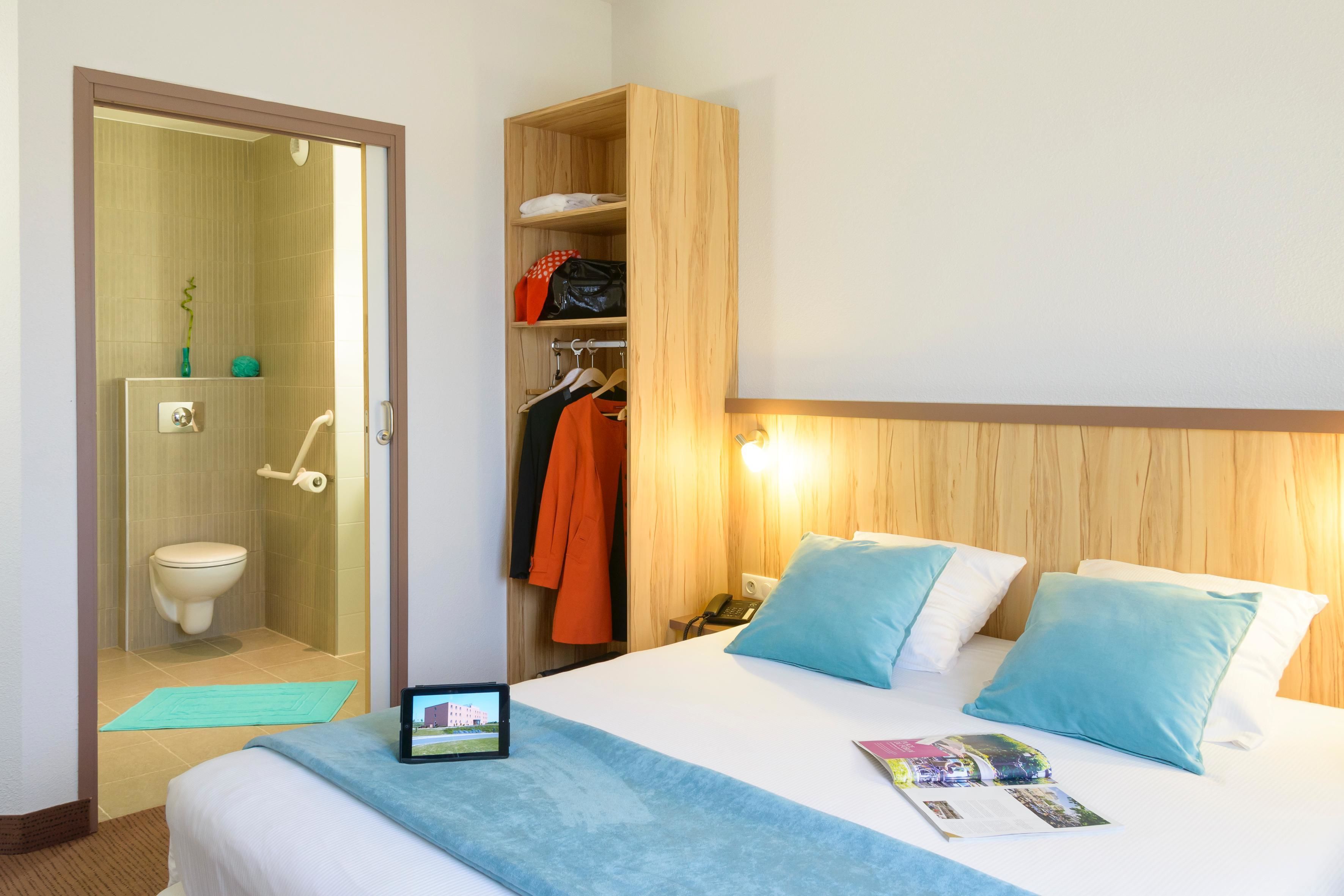 Una habitación de hotel con cama, mesita de noche, armario de madera y baño con inodoro y ducha.