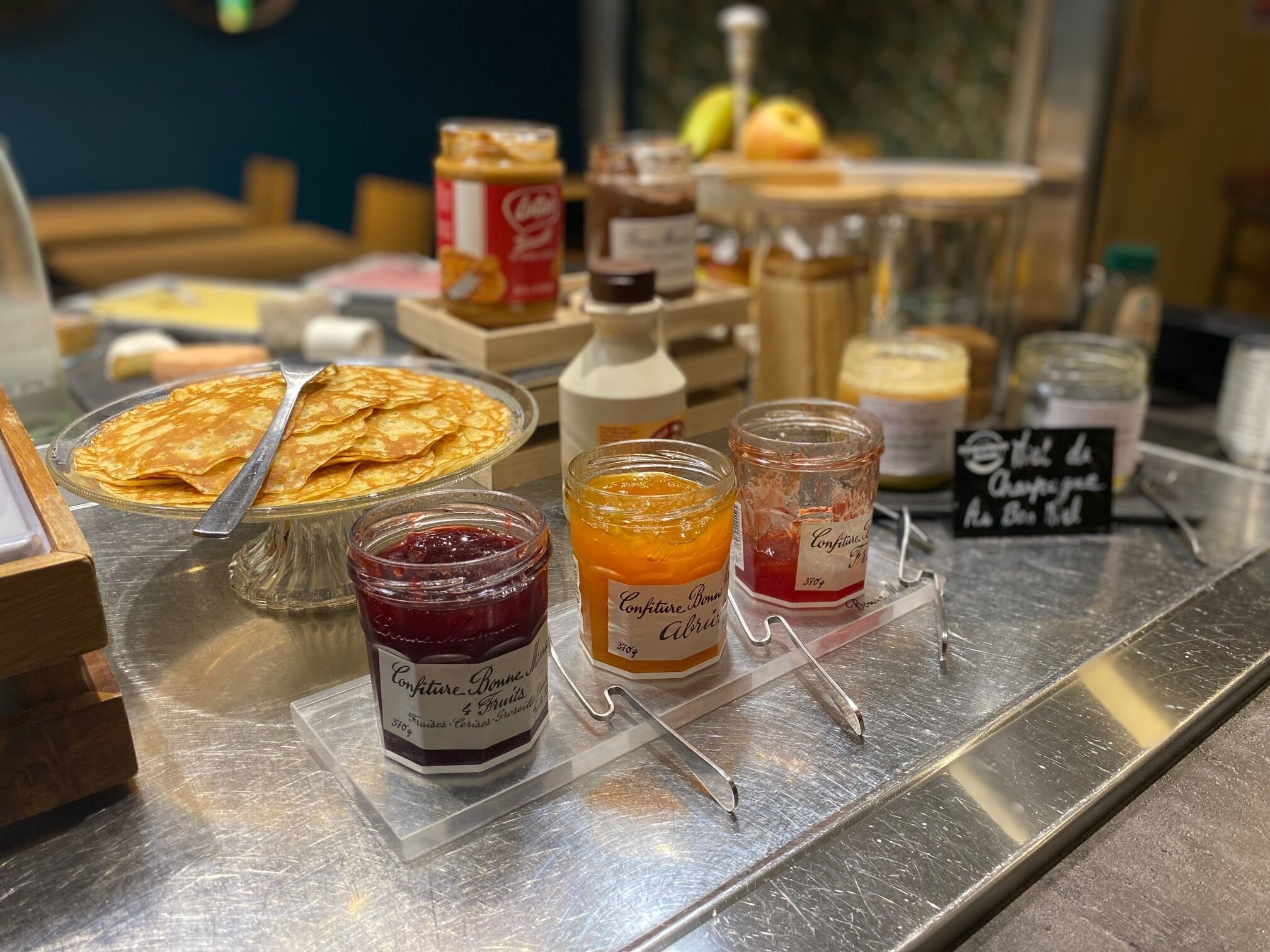 Un buffet de petit-déjeuner avec différentes sortes de confitures, une bouteille de lait et une assiette de crêpes.