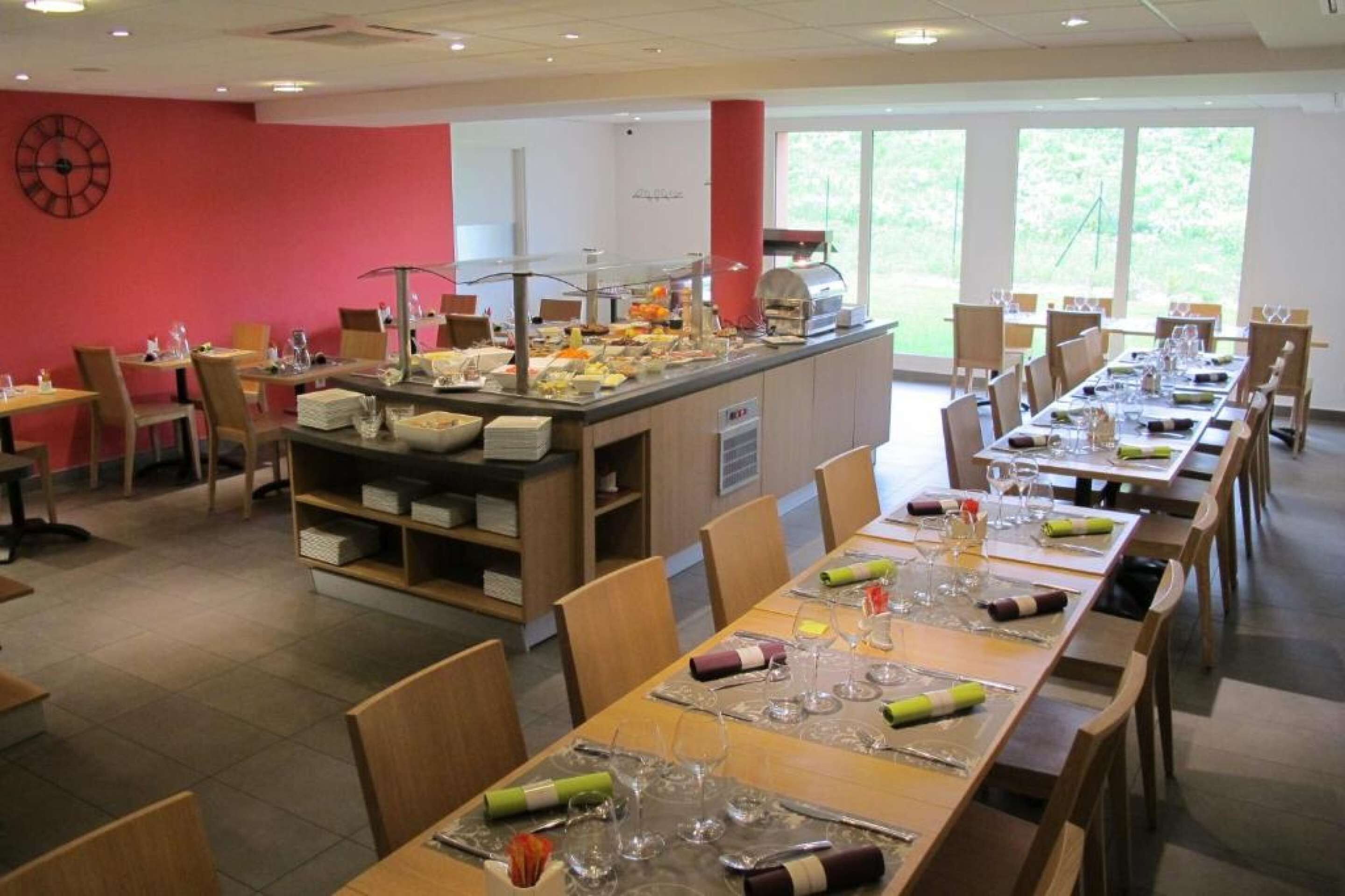 A buffet-style restaurant with multiple dining tables, a central serving station, and a large window providing a view of the outdoors.